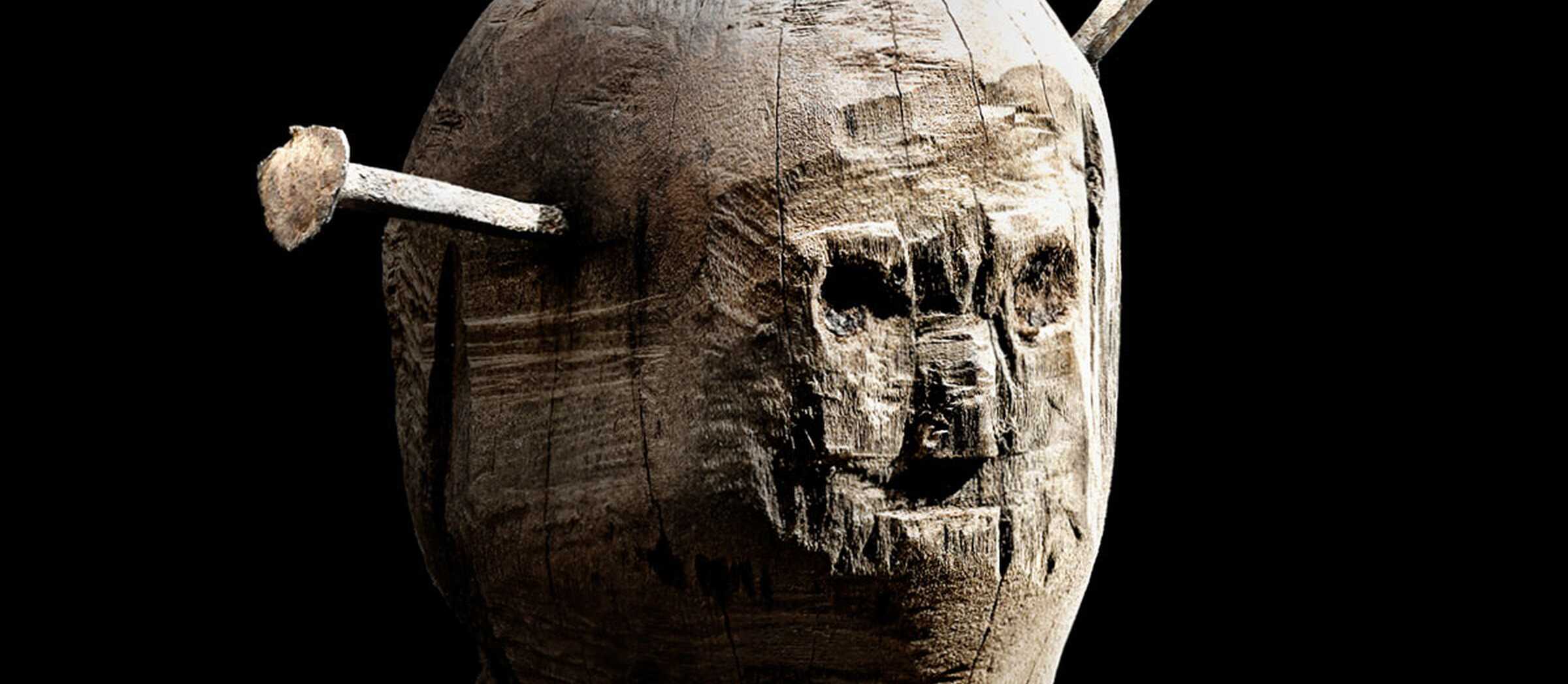 Darstellung einer sogenannten Nagelpuppe, einer Holzfigur in Form eines Menschen mit angedeutetem Gesicht und Eisennägeln, die in den "Kopf" gehämmert wurden.